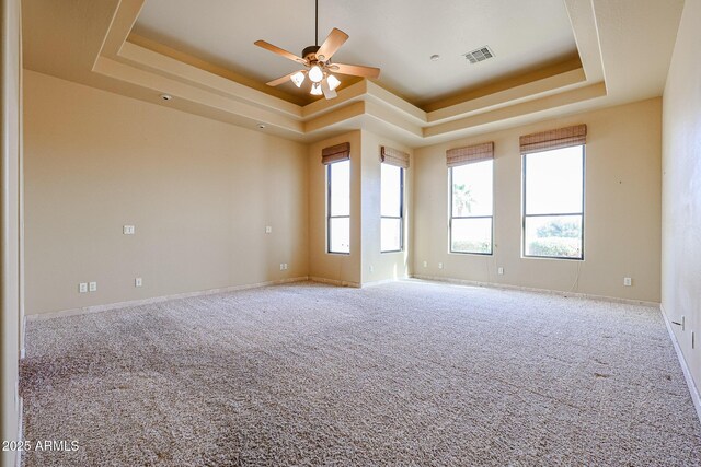 empty room featuring ceiling fan, a tray ceiling, and carpet