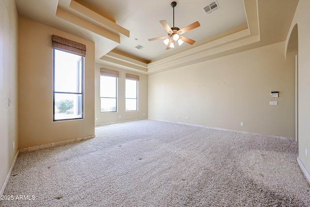 carpeted spare room with a raised ceiling and ceiling fan