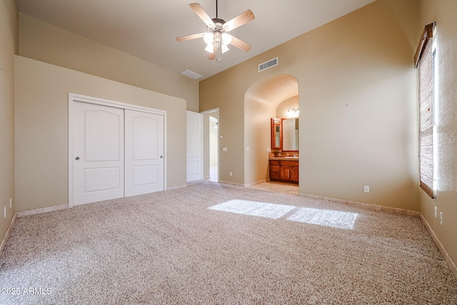 unfurnished bedroom featuring ceiling fan, a towering ceiling, connected bathroom, light carpet, and a closet