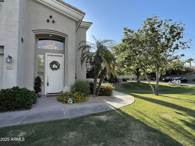 entrance to property featuring stucco siding and a lawn