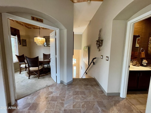 foyer entrance with a chandelier, baseboards, carpet, stone finish flooring, and arched walkways
