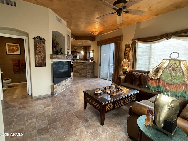 living room with ceiling fan, stone finish flooring, arched walkways, and baseboards