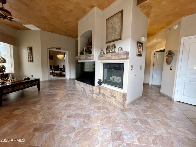 living area with arched walkways, a multi sided fireplace, ceiling fan, and baseboards