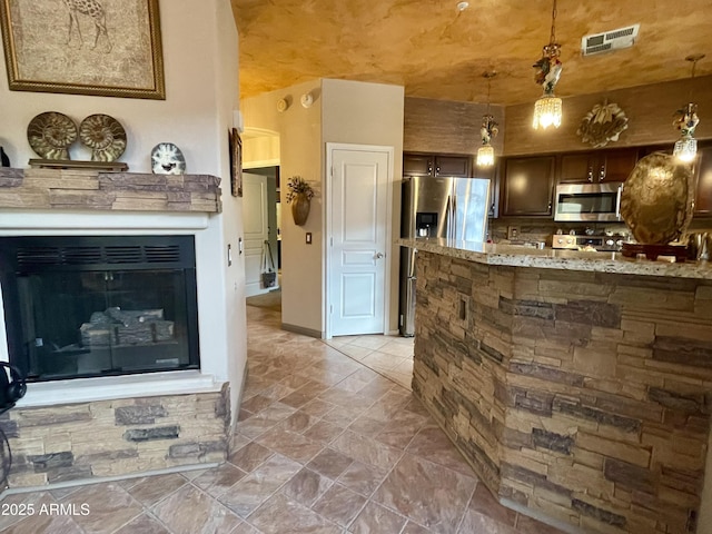kitchen with appliances with stainless steel finishes, decorative light fixtures, a fireplace, stone finish flooring, and light stone countertops
