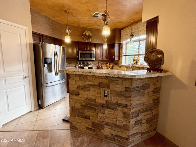 kitchen featuring appliances with stainless steel finishes, pendant lighting, light stone counters, a peninsula, and light tile patterned floors
