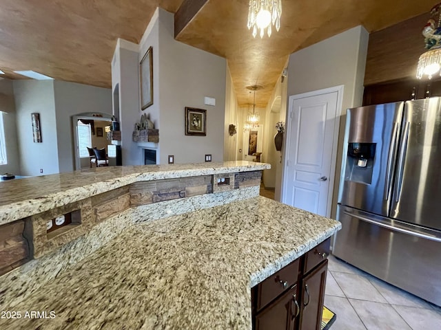 kitchen with stainless steel fridge, arched walkways, light tile patterned floors, and light stone counters