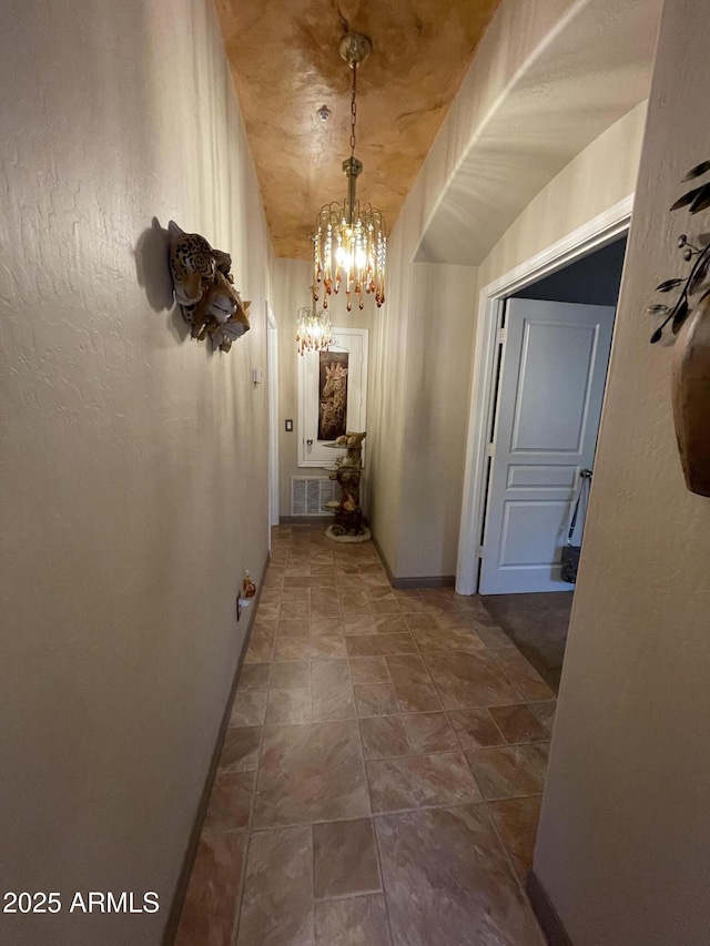 hallway featuring a chandelier, baseboards, and dark stone finish floors