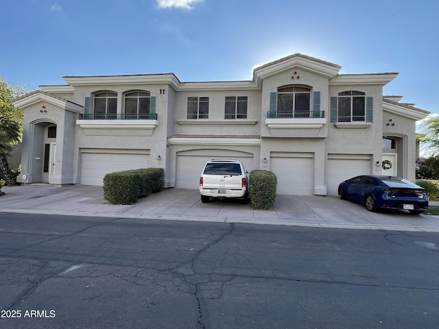 view of front of home with an attached garage, driveway, stucco siding, and a balcony