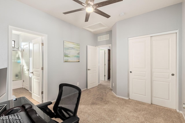 office space featuring light colored carpet, a ceiling fan, baseboards, visible vents, and attic access