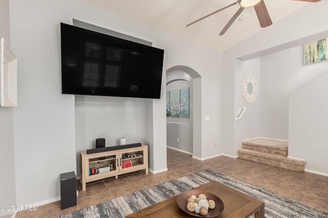 tiled living area with stairs, arched walkways, a ceiling fan, and baseboards