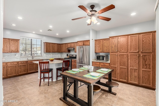 kitchen with under cabinet range hood, a sink, appliances with stainless steel finishes, brown cabinets, and decorative backsplash