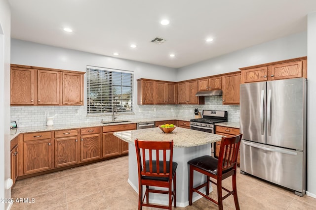 kitchen featuring brown cabinets, appliances with stainless steel finishes, a sink, a kitchen island, and under cabinet range hood