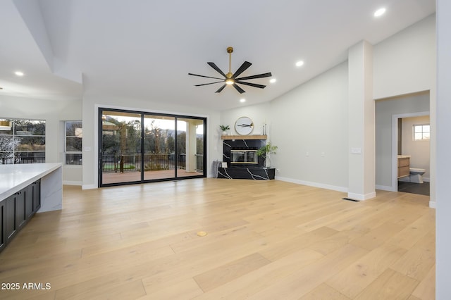 unfurnished living room featuring ceiling fan, a fireplace, light hardwood / wood-style floors, and a healthy amount of sunlight