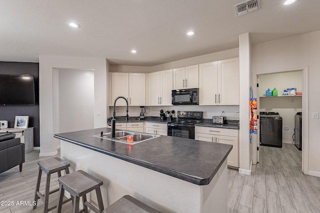 kitchen featuring a sink, visible vents, black appliances, washer and clothes dryer, and dark countertops