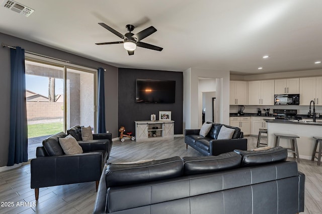 living room featuring light wood-style floors, visible vents, ceiling fan, and baseboards