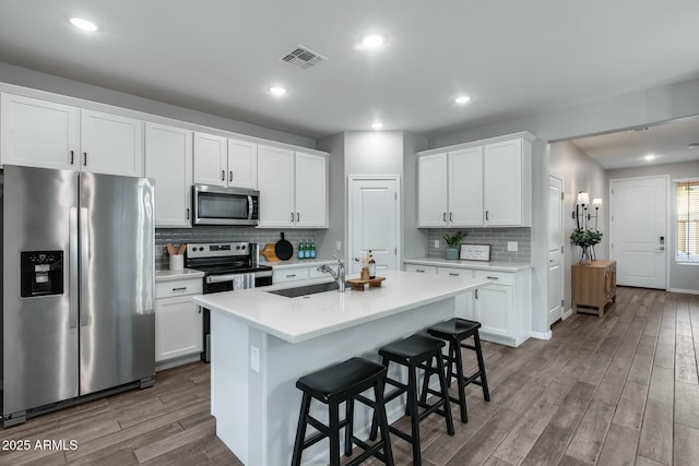 kitchen featuring a kitchen island with sink, white cabinets, sink, a kitchen bar, and stainless steel appliances