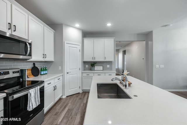 kitchen with sink, stainless steel appliances, backsplash, light hardwood / wood-style floors, and white cabinets