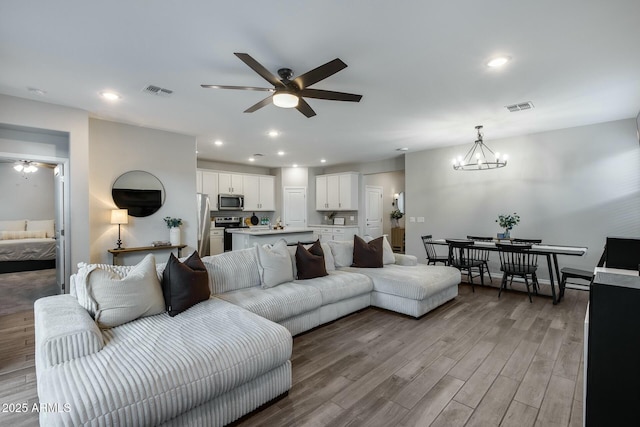 living room featuring ceiling fan with notable chandelier and light wood-type flooring