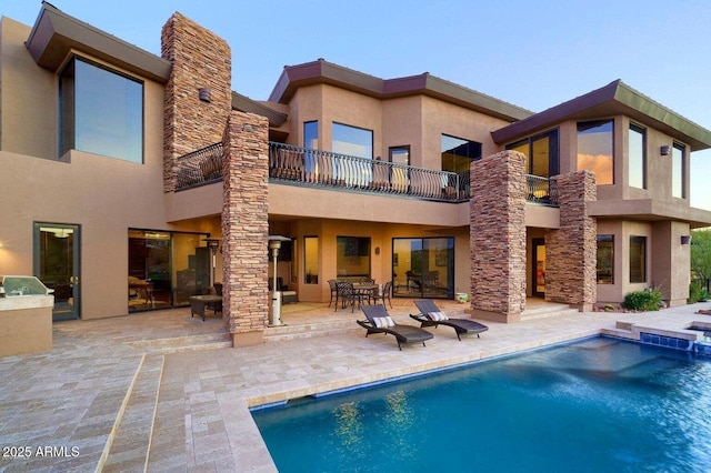 rear view of property featuring a balcony, a patio area, stone siding, and stucco siding