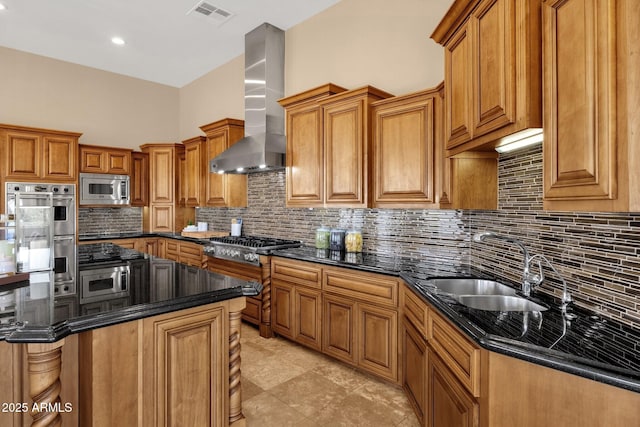 kitchen featuring visible vents, brown cabinets, a sink, appliances with stainless steel finishes, and wall chimney exhaust hood