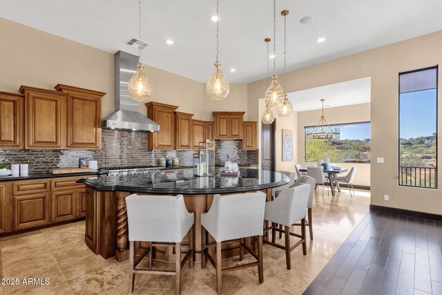 kitchen featuring visible vents, brown cabinets, a spacious island, a breakfast bar area, and wall chimney exhaust hood