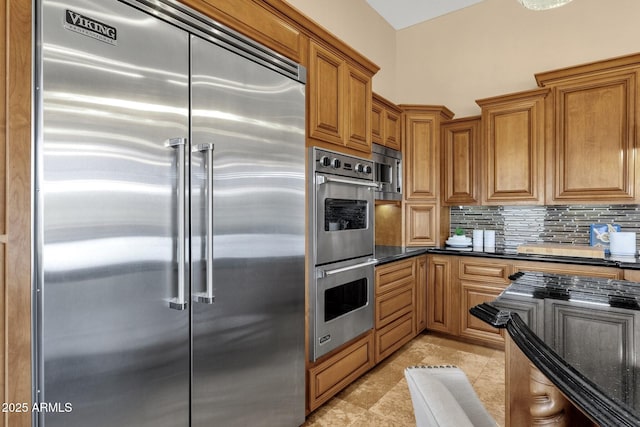 kitchen with decorative backsplash, dark stone countertops, brown cabinets, and appliances with stainless steel finishes