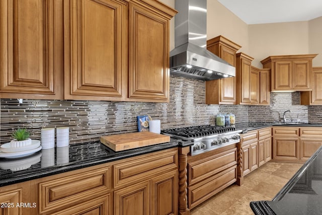 kitchen with dark stone countertops, a sink, stainless steel gas stovetop, wall chimney range hood, and backsplash