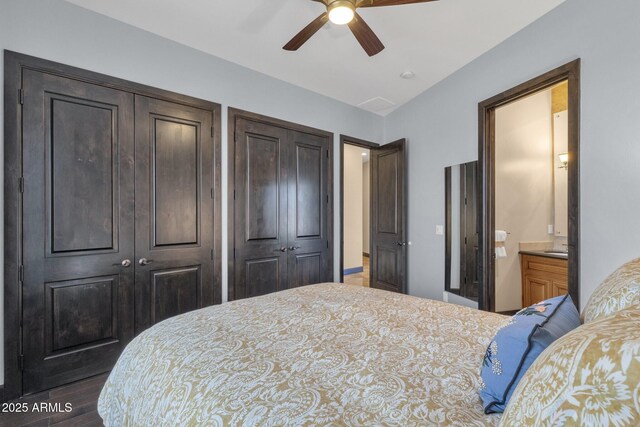 bedroom featuring dark wood finished floors, ensuite bathroom, a ceiling fan, and two closets