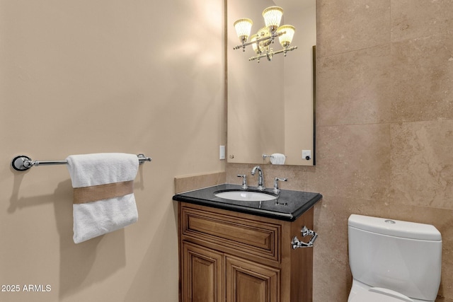 half bath featuring tile walls, a notable chandelier, toilet, and vanity