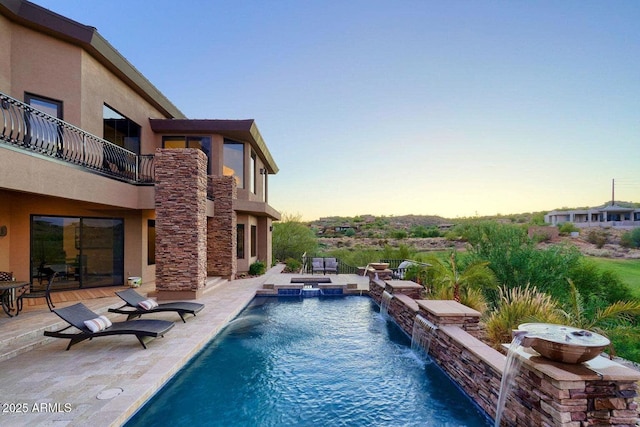 pool at dusk with a patio area and a pool with connected hot tub