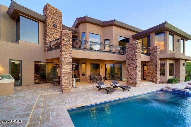 rear view of house featuring stucco siding, stone siding, a balcony, and a patio area