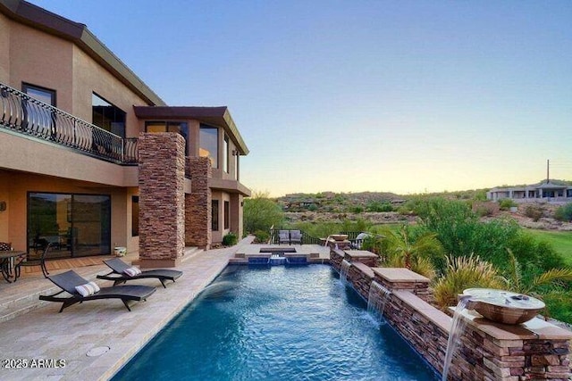 pool at dusk with a pool with connected hot tub and a patio