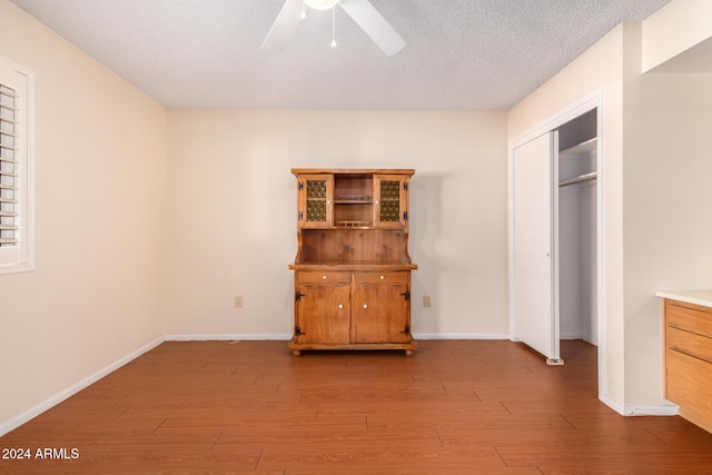 unfurnished bedroom featuring ceiling fan, a closet, a textured ceiling, and light wood-type flooring