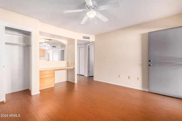 unfurnished bedroom featuring wood-type flooring, built in desk, a textured ceiling, and ceiling fan