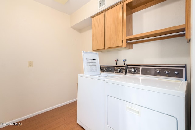 laundry room with cabinets, light wood-type flooring, and washing machine and clothes dryer