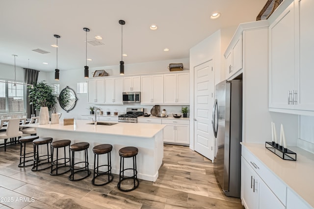 23032 E Roundup Way, Queen Creek, AZ 85142 - kitchen with stainless steel appliances, a kitchen bar, white cabinetry, an island with sink, and decorative light fixtures