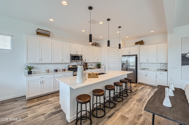 23032 E Roundup Way, Queen Creek, AZ 85142 - kitchen with appliances with stainless steel finishes, a breakfast bar, an island with sink, white cabinetry, and light wood finished floors
