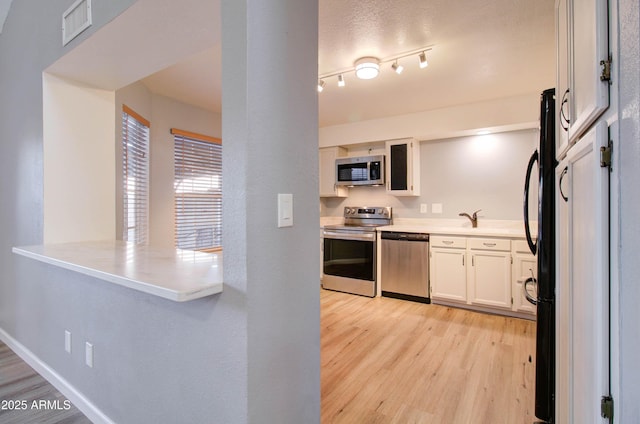 kitchen featuring light wood-type flooring, appliances with stainless steel finishes, a textured ceiling, and white cabinetry