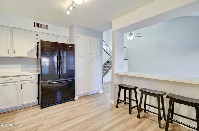 kitchen with black fridge, ceiling fan, light wood-type flooring, a kitchen bar, and white cabinetry