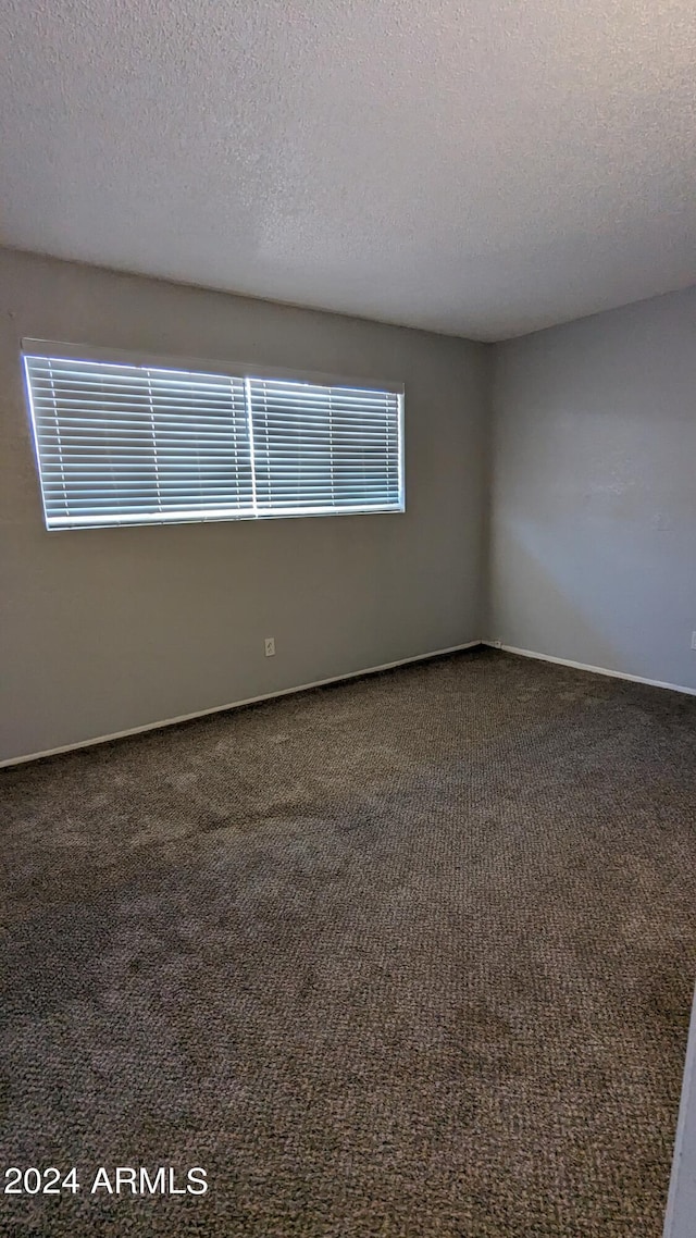 unfurnished room featuring dark colored carpet and a textured ceiling