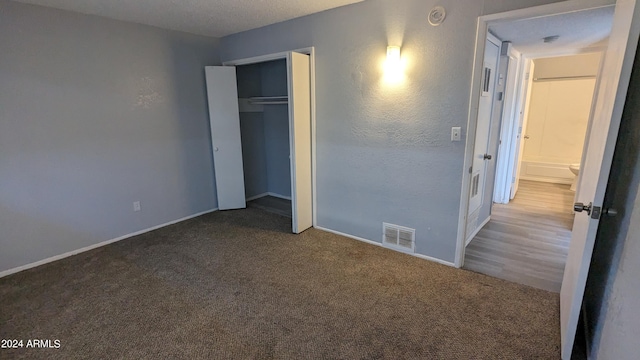 unfurnished bedroom featuring a textured ceiling, a closet, and dark carpet