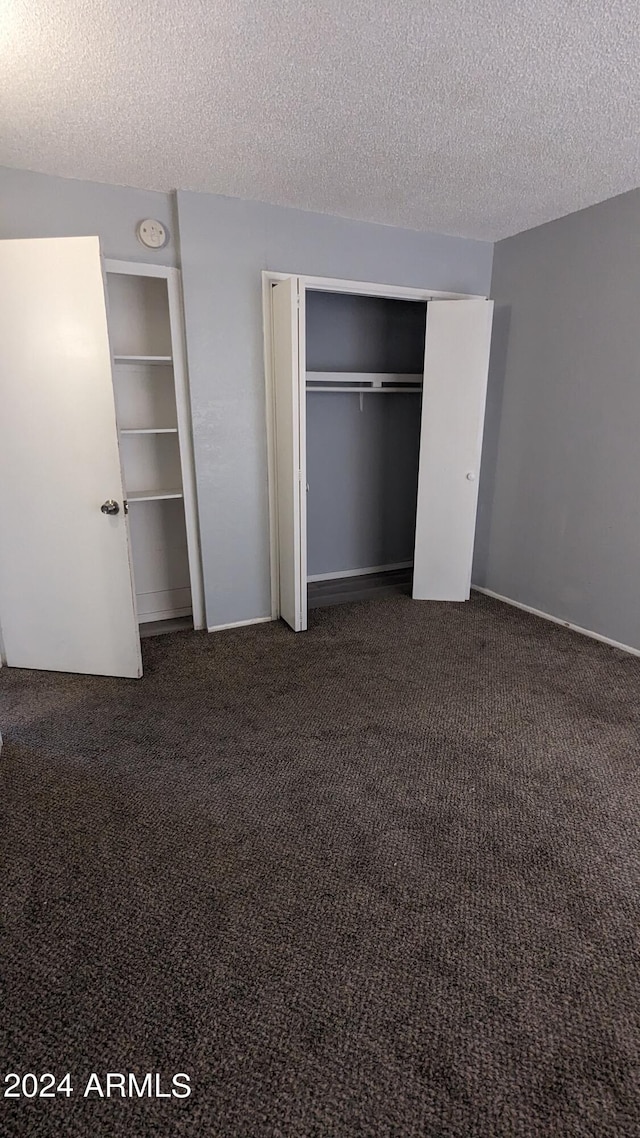 unfurnished bedroom featuring a textured ceiling and dark carpet