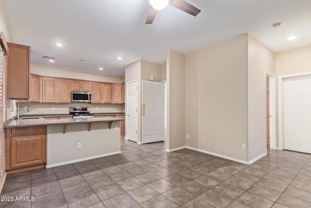 kitchen with appliances with stainless steel finishes, sink, kitchen peninsula, ceiling fan, and a breakfast bar