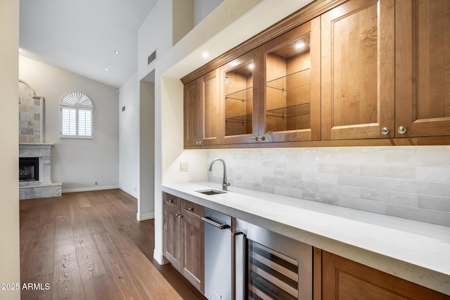 bar with sink, beverage cooler, backsplash, a premium fireplace, and light hardwood / wood-style flooring