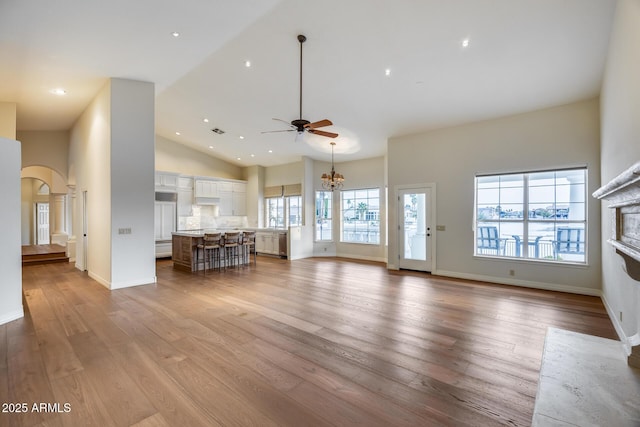 unfurnished living room featuring high vaulted ceiling, ceiling fan with notable chandelier, and light hardwood / wood-style floors