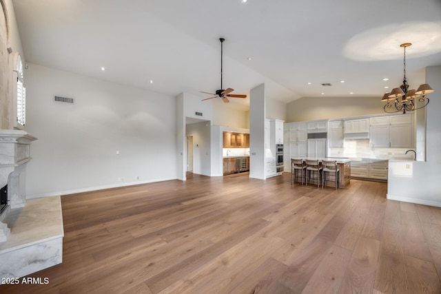 unfurnished living room with high vaulted ceiling, ceiling fan with notable chandelier, and light hardwood / wood-style flooring