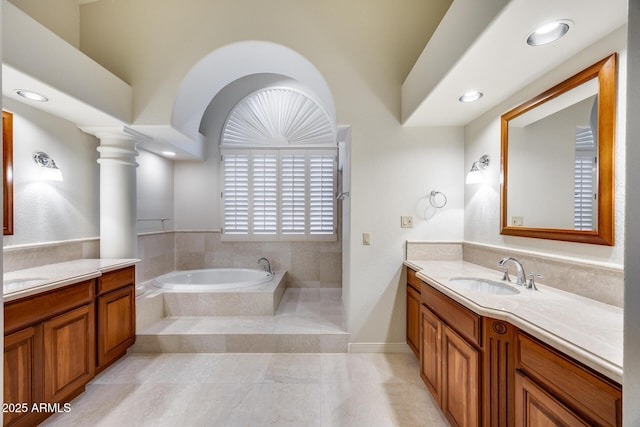 bathroom featuring decorative columns, vanity, and a relaxing tiled tub