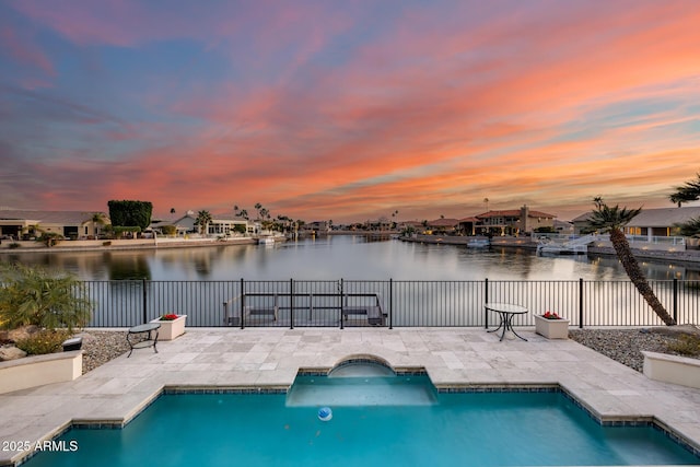 pool at dusk featuring a water view and a patio