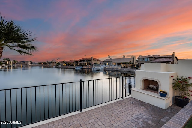 patio terrace at dusk with a water view and an outdoor fireplace