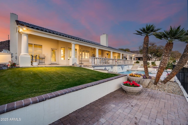 back house at dusk featuring a fenced in pool, a lawn, and a patio area